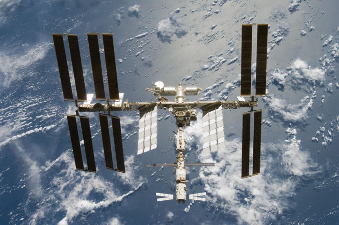 Station spatiale internationale en orbite au‑dessus de la Terre, avec ses modules et panneaux solaires visibles.